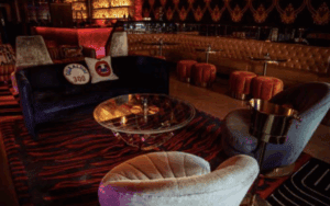 Elegant lounge with velvet seating, gold accents, and a cozy bar in warm ambient lighting.